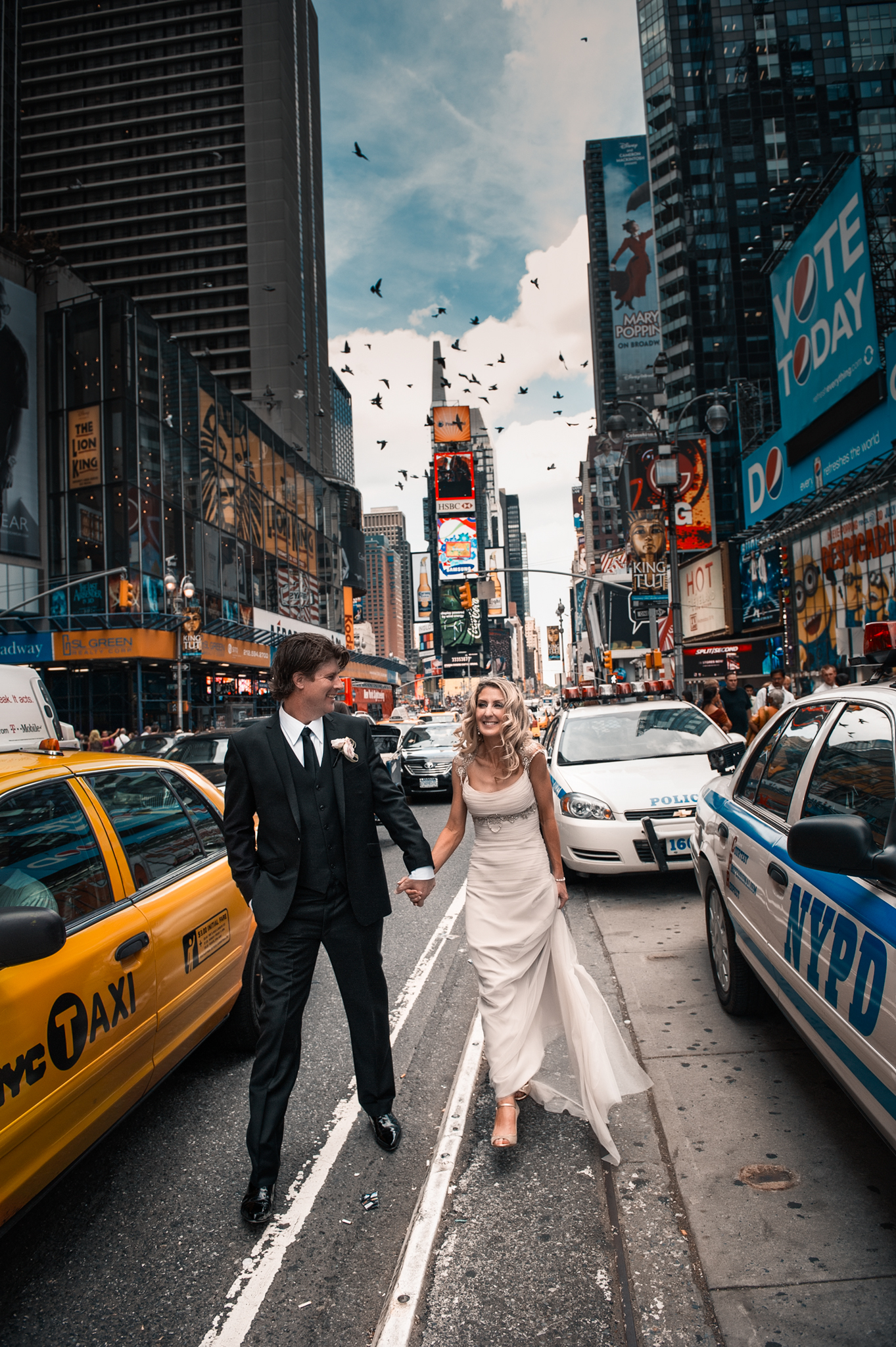 Happy wedding couple walk hand in hand through the streets of New York City between an iconic yellow can and NYPD car