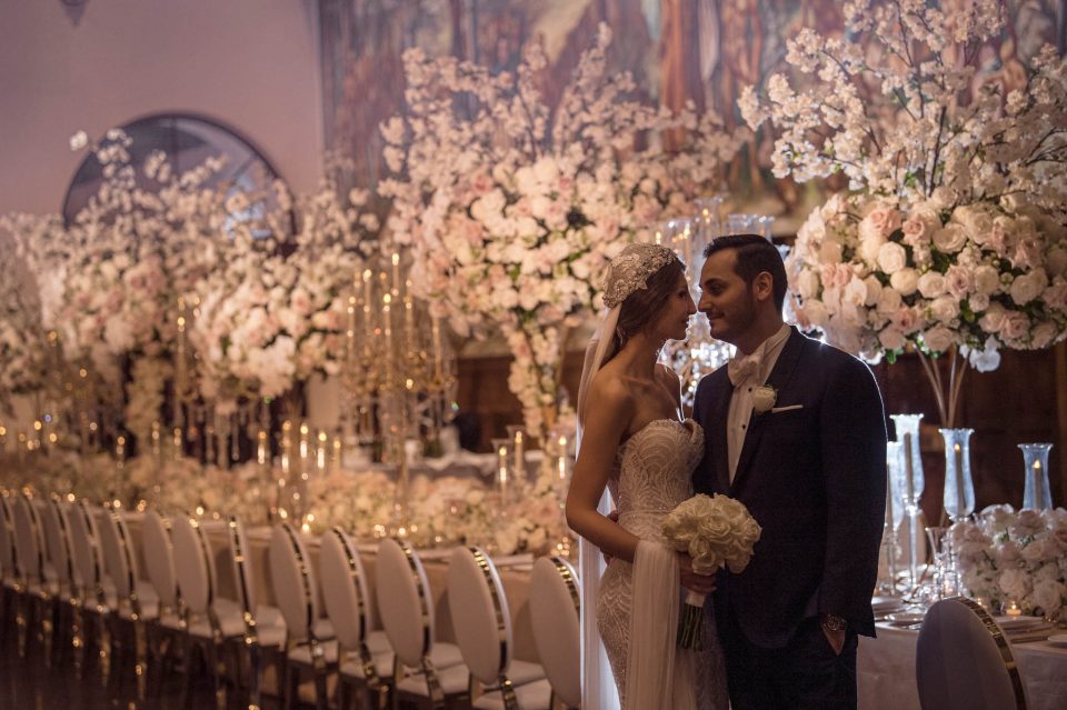 wedding couple posed with john emmanuel floral arrangement behind