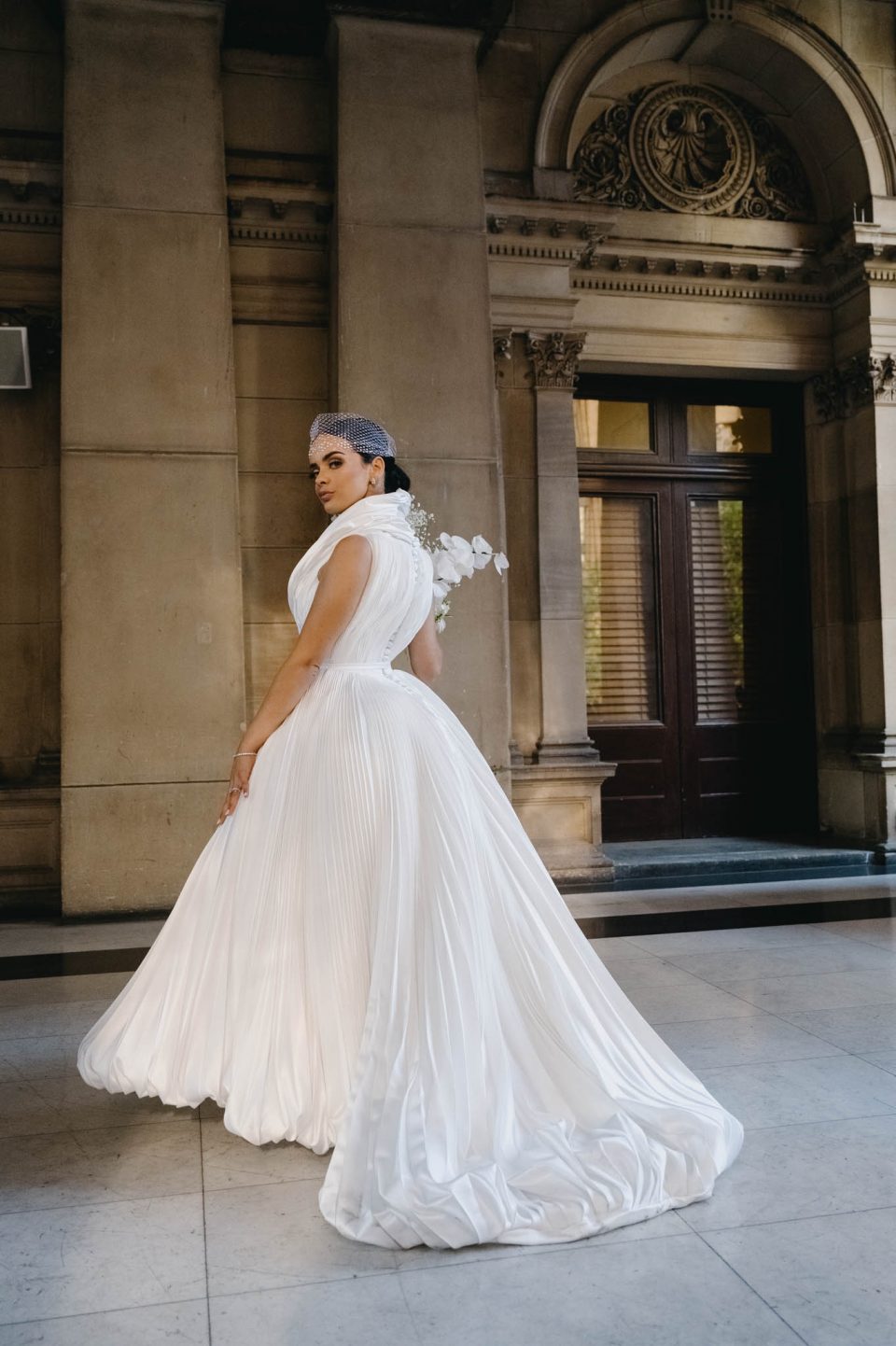 Bride in J’aton couture gown looking over shoulder on balcony of Melbourne town hall