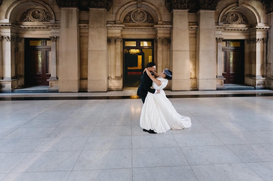 Bride and groom embraced, looking at each other framed by the Victorian style architecture