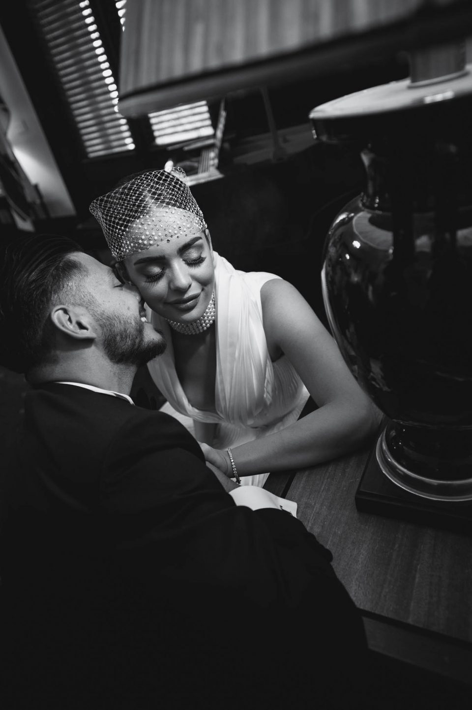 Groom kisses brides ear as she looks down lit by the lamp in the foreground
