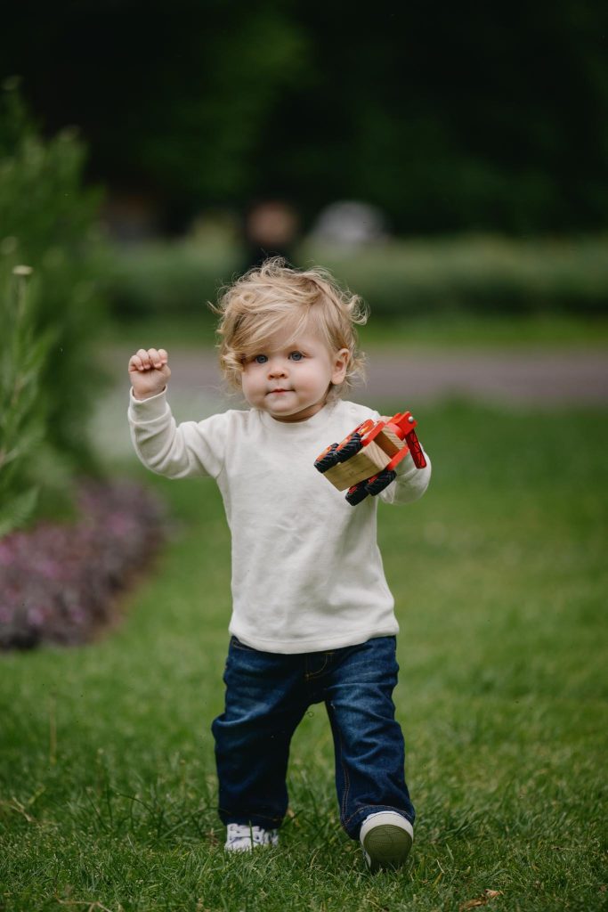 portrait photo of toddler walking with toy in carlton gardens