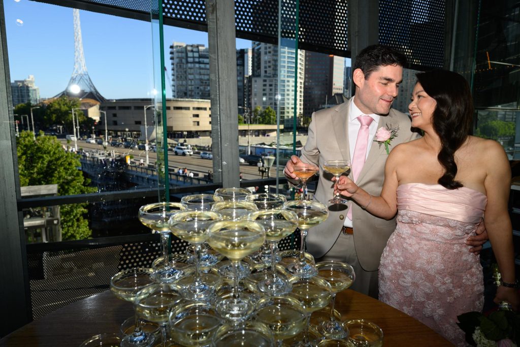 Bride and groom toast with Champagne tower with Melbourne skyline views at Transport Hotel wedding