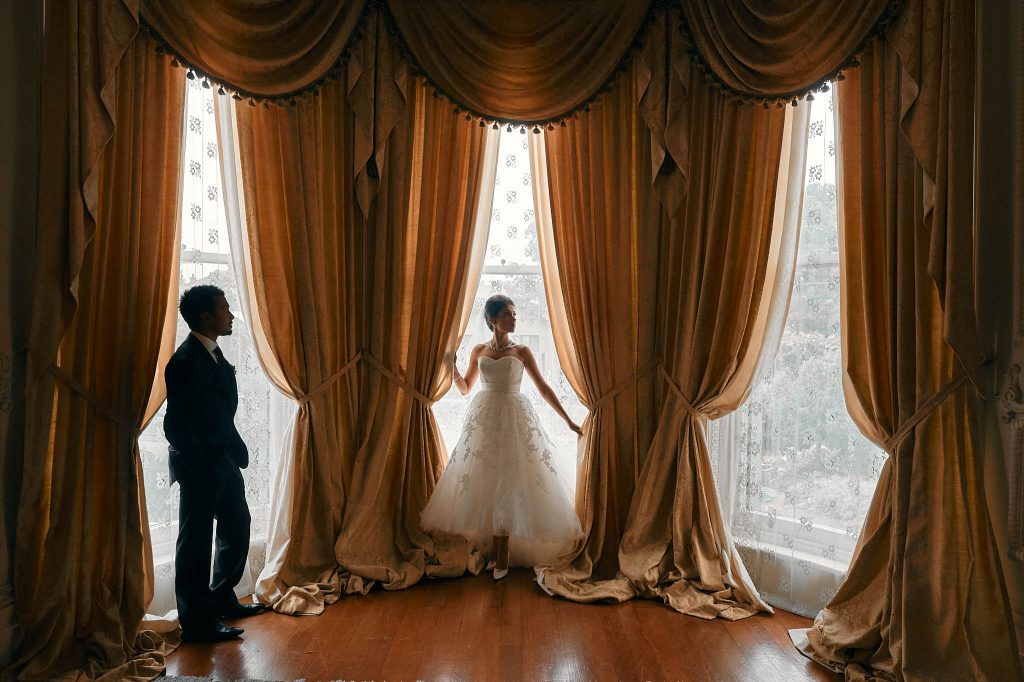 Bride and groom standing before the grand windows of Labassa Mansion, captured in an elegant editorial wedding photograph.